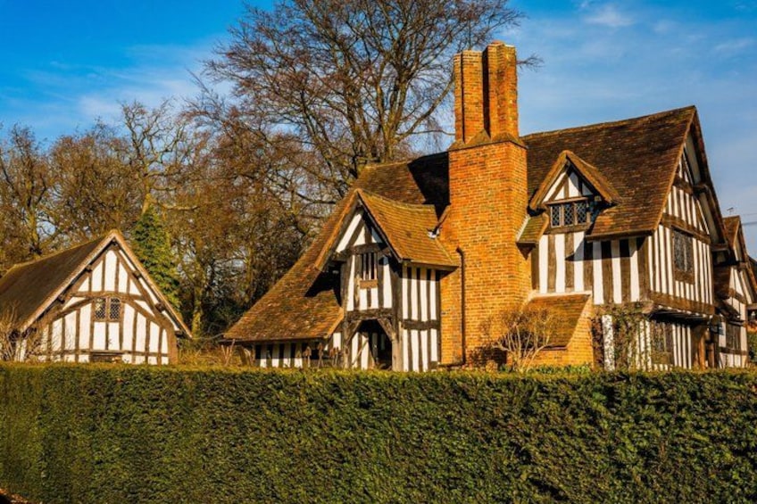 A Tudor-style house with a brick chimney, surrounded by a hedge and trees. 5