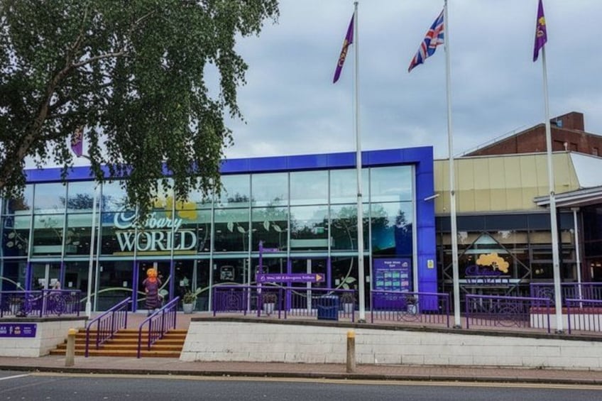 A Cadbury World building with a glass facade, purple accents, and a set of stairs leading up to the entrance. 1