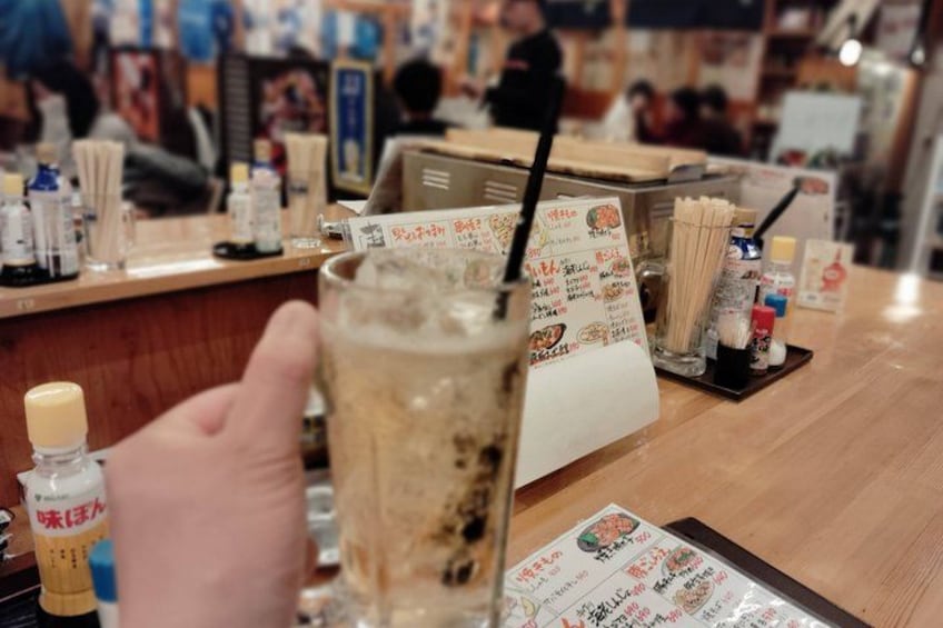 A bar counter with a drink in a glass, menu, condiments, and a person holding a menu. 3