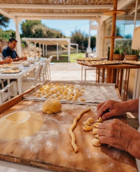 A person shaping dough on a wooden surface, with a table of uncooked dough in the background. 5