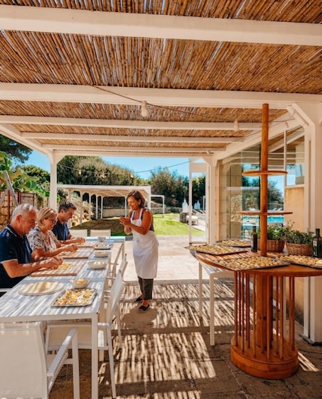 An outdoor dining area with a thatched roof, tables with food, and a person serving. 1