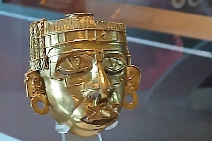 A gold-colored, intricately designed object with a face, possibly a historical artifact. 5
