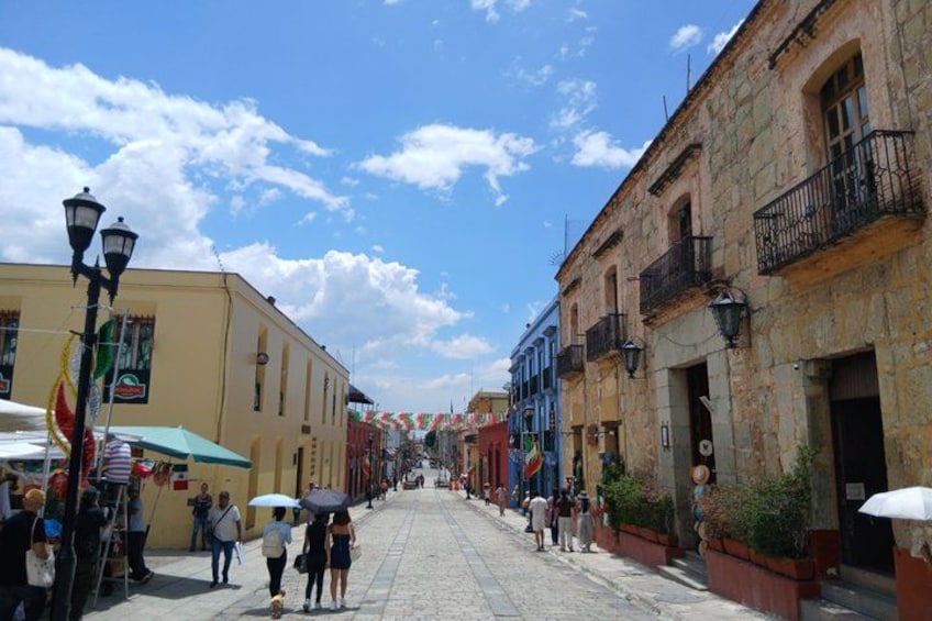 A cobblestone street lined with historic buildings, a clear sky, and pedestrians. 1