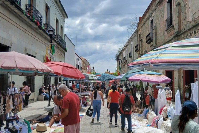 A bustling outdoor market with people shopping and vendors selling goods under colorful umbrellas. 3