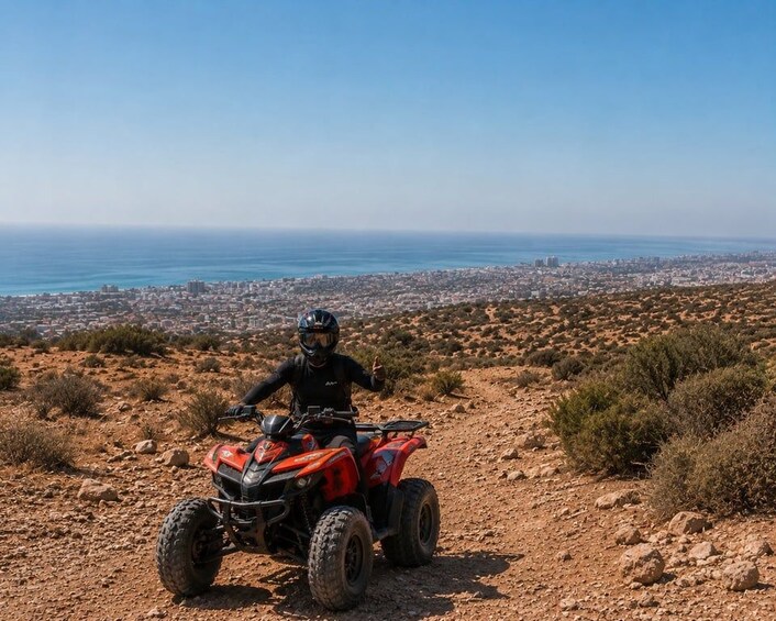 A person riding an ATV on a rocky trail with a city and ocean in the background. 3