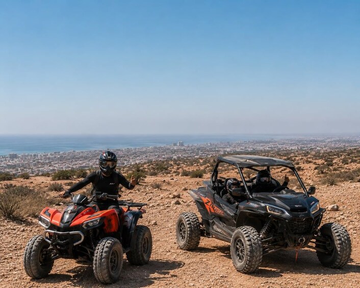 Two off-road vehicles on a dirt path with a cityscape in the background. 1