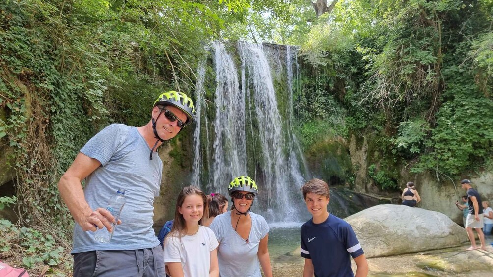 A waterfall in a lush, green forest setting with people standing around. 4