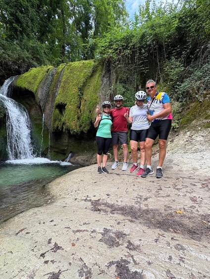 Four people standing on a rocky shore with a waterfall in the background. 2