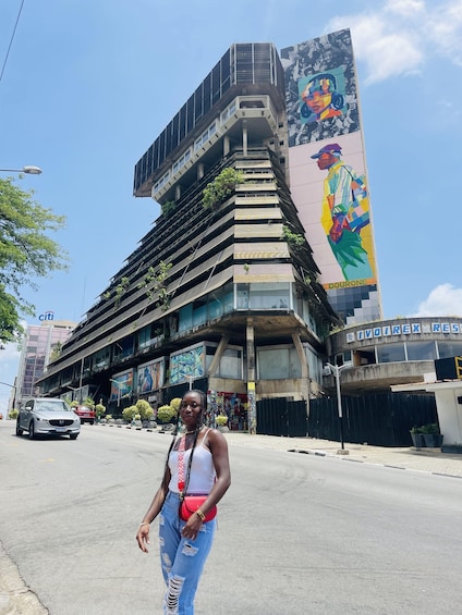 A modern building with a colorful mural, a street with cars, and a person standing in front. 1