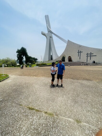 A modern architectural structure with a unique design, a paved area with people, and a clear sky. 2