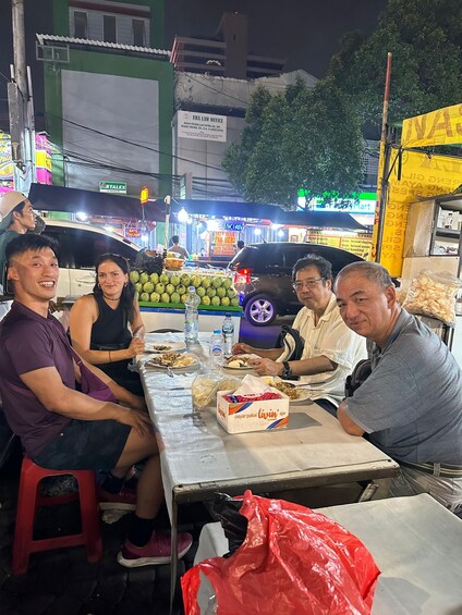 Un grupo de personas cenando en un mercado al aire libre, con comida y bebidas sobre la mesa. 5