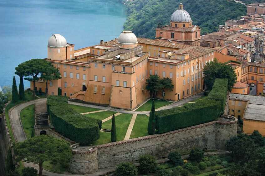 A historic building with domed structures, surrounded by a well-maintained garden and a stone wall. 1
