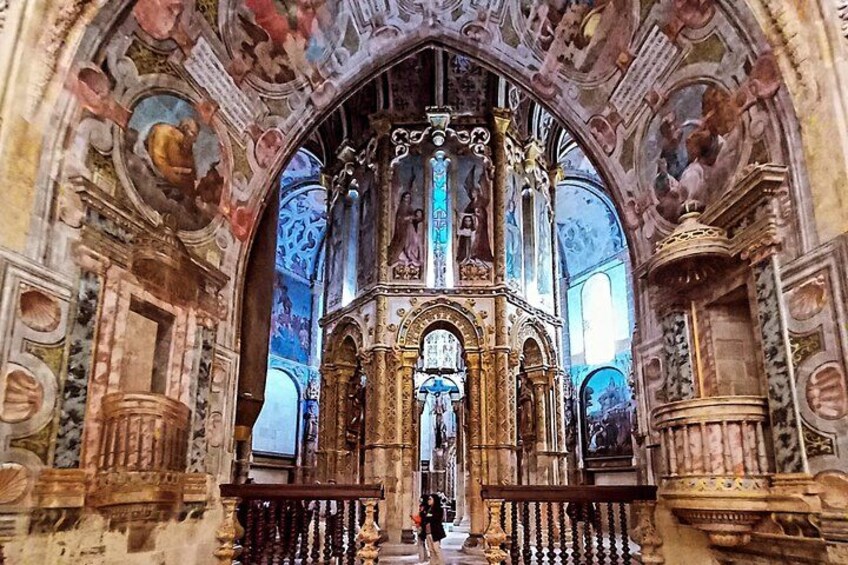 An ornate church interior with detailed frescoes, a central altar, and a large crucifix. 3
