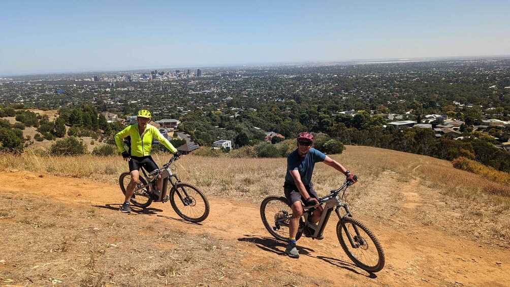 Two cyclists on a dirt path with a cityscape in the background. 5