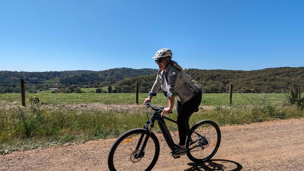 A person riding a mountain bike on a dirt path with a hilly landscape in the background. 3