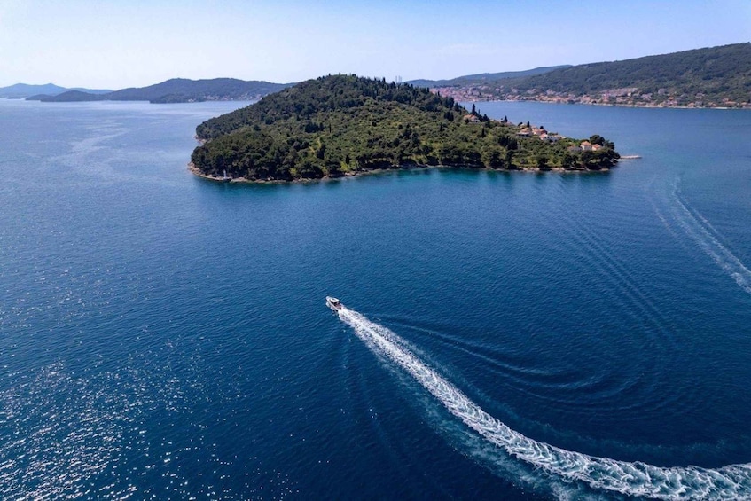 A small island surrounded by a calm sea, with a boat creating a wake. 5
