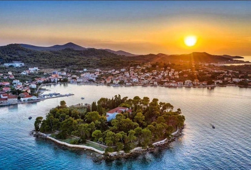 A coastal town at sunset with a small island in the foreground. 1