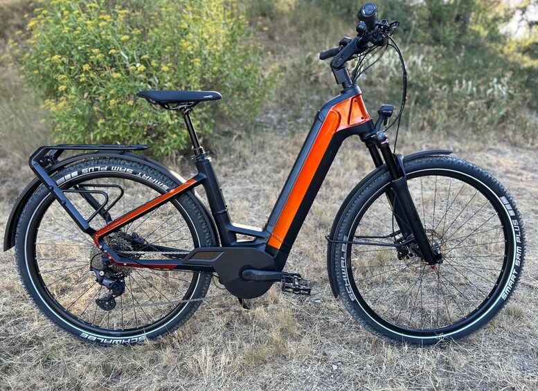 A stationary electric bicycle with a black and orange frame, a rear rack, and thick tires. 4