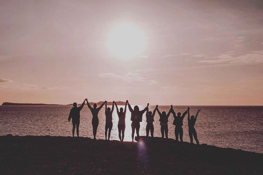 Un gruppo di persone in spiaggia con le braccia alzate, in controluce al tramonto. 4