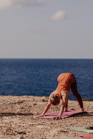Una persona esegue una posa yoga su un tappetino rosa su una spiaggia rocciosa, con l'oceano sullo sfondo. 5