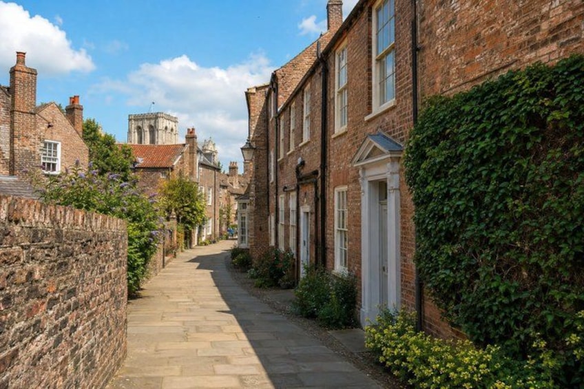 A narrow brick street lined with traditional houses, a stone wall on one side, and a tower in the distance. 5