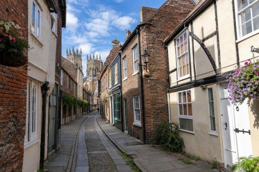 A narrow cobblestone street flanked by historic buildings with a church spire in the distance. 4