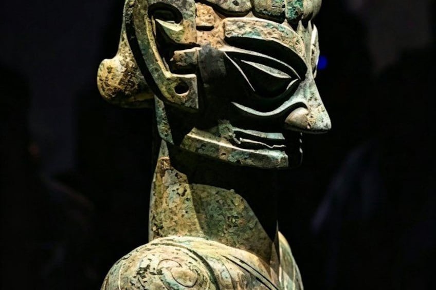 A bronze statue with a mask-like face and intricate patterns on its surface. 1