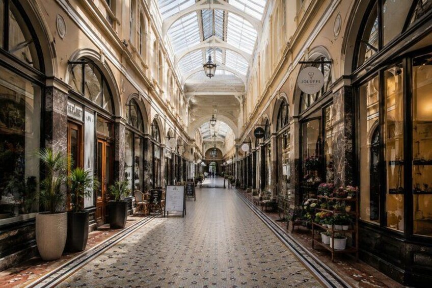 A covered shopping corridor with arched ceilings, potted plants, and storefronts. 4