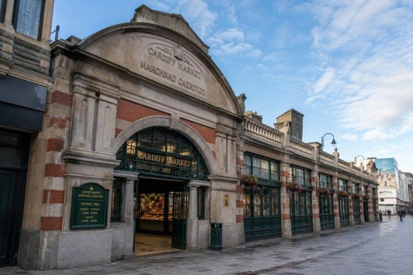 The exterior of the Cardiff Market, a historic market building with a prominent archway and green awnings. 3