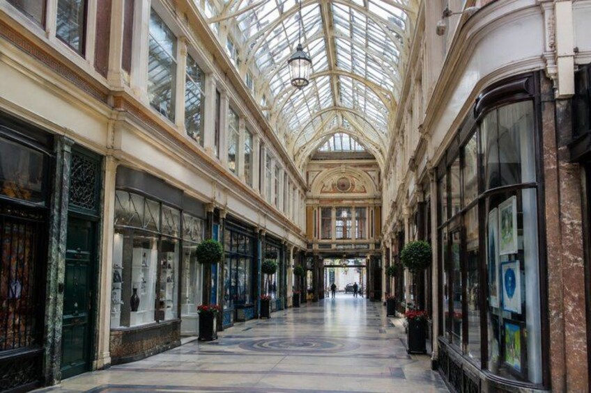A covered shopping corridor with glass ceilings, marble floors, and storefronts. 2