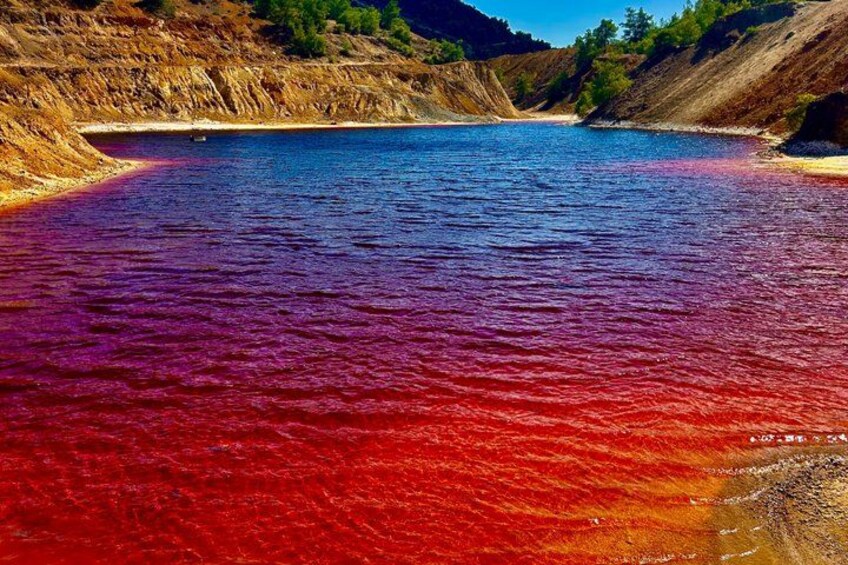 A river with red and blue water, surrounded by cliffs and sparse vegetation. 1