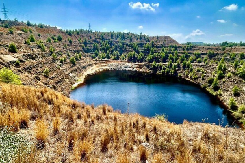 A lake surrounded by dry grassland and sparse trees, with a hilly landscape in the background. 2