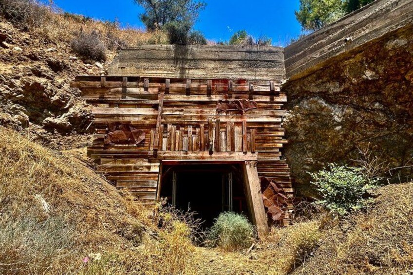 An old wooden structure with a staircase leading up to a door, surrounded by dry grass and shrubs. 5