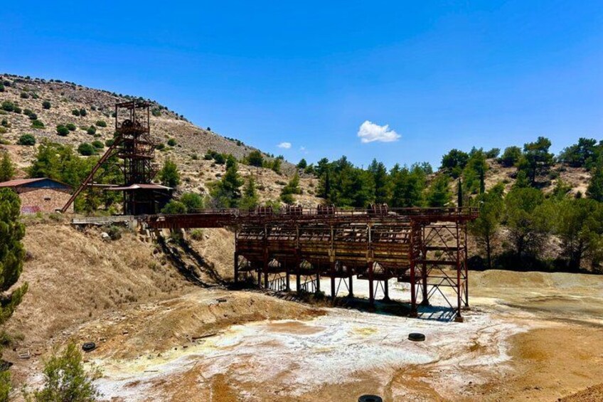 An abandoned industrial structure with a metal framework, a hillside in the background, and a clear sky. 4