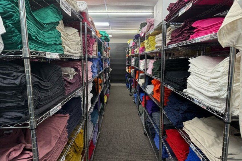A clothing store aisle with shelves stocked with folded clothes in various colors. 3