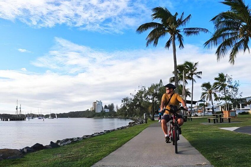 A person riding a bicycle along a waterfront path with palm trees and a marina in the background. 3