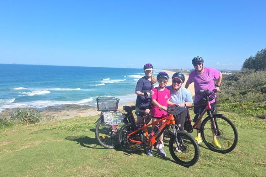 A group of people with bicycles on a grassy area near the ocean. 1