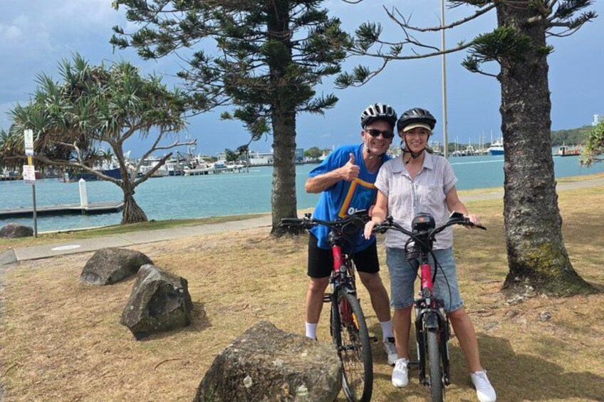 Two people on bicycles, a body of water, and a marina with boats. 4