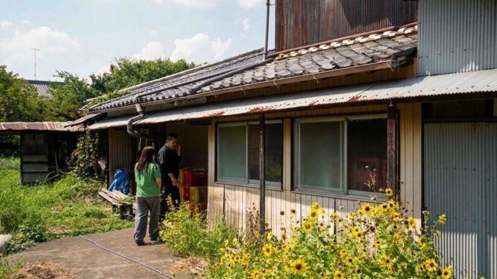 A rustic building with a corrugated metal roof, a wooden porch, and a garden with yellow flowers. 2