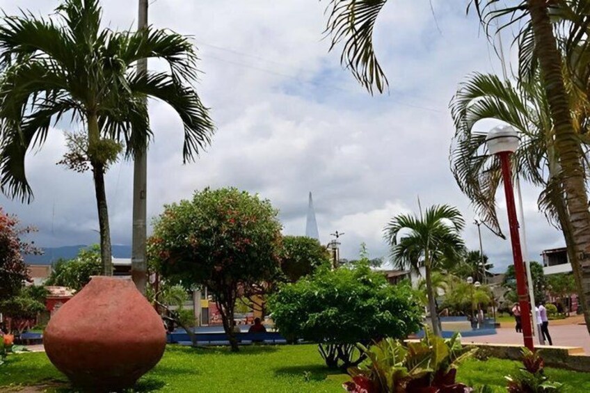 A park with palm trees, a large red vase, and a distant church spire. 5