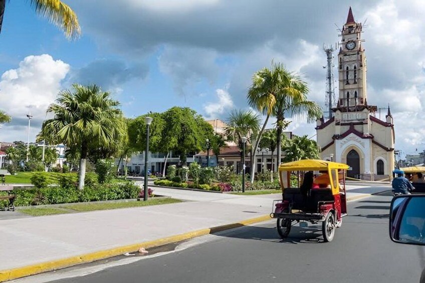A street with a yellow and red vehicle, palm trees, and a clock tower. 2