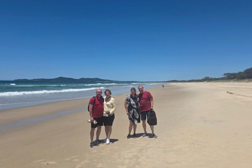 A beach with three people standing, one holding a camera. 5