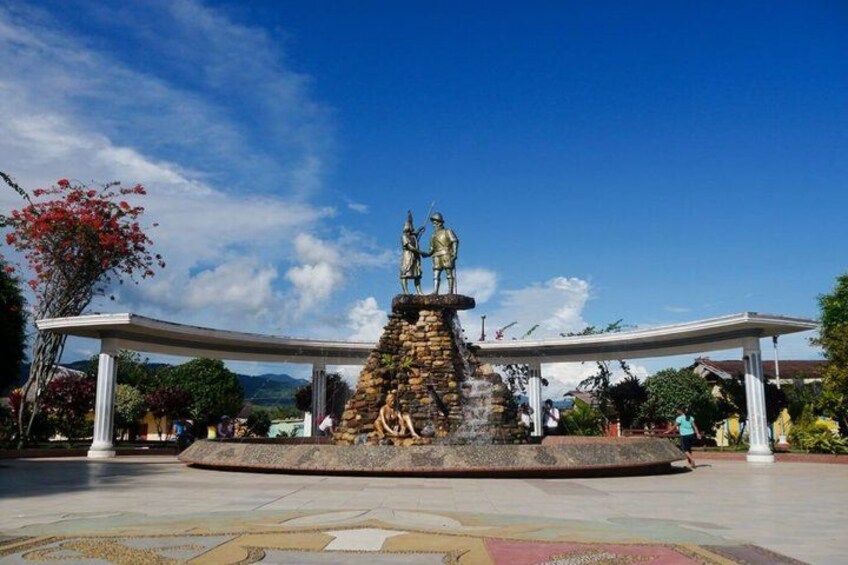 A statue on a pedestal with two figures, surrounded by a stone base and a fountain. 3