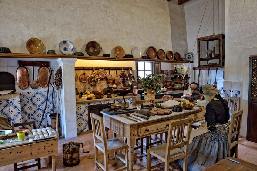 A rustic kitchen with wooden furniture, hanging pots, and a variety of dishes on shelves. 2