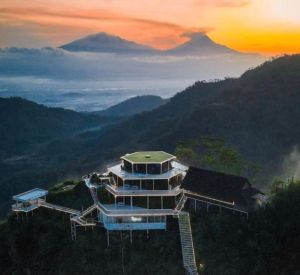 A multi-level building with a green roof, surrounded by mountainous terrain and a sunset sky. 1