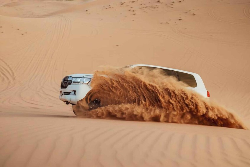 Un veicolo bianco che si muove in un paesaggio desertico sabbioso con dune ondulate. 1