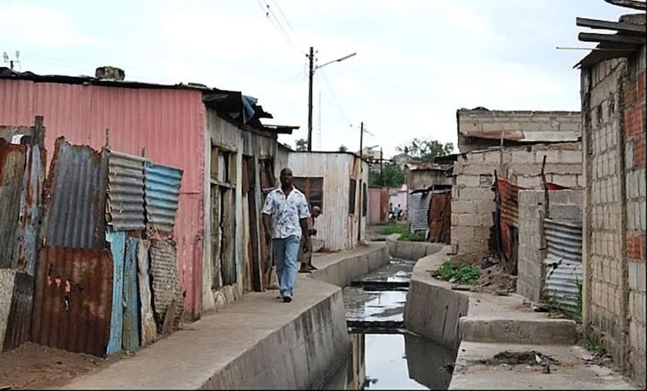 A narrow alley with corrugated metal buildings, a man walking, and a small water channel. 3
