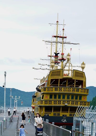 A large, ornate ship named 'Queen Ashinoko' docked at a pier with people walking around. 2