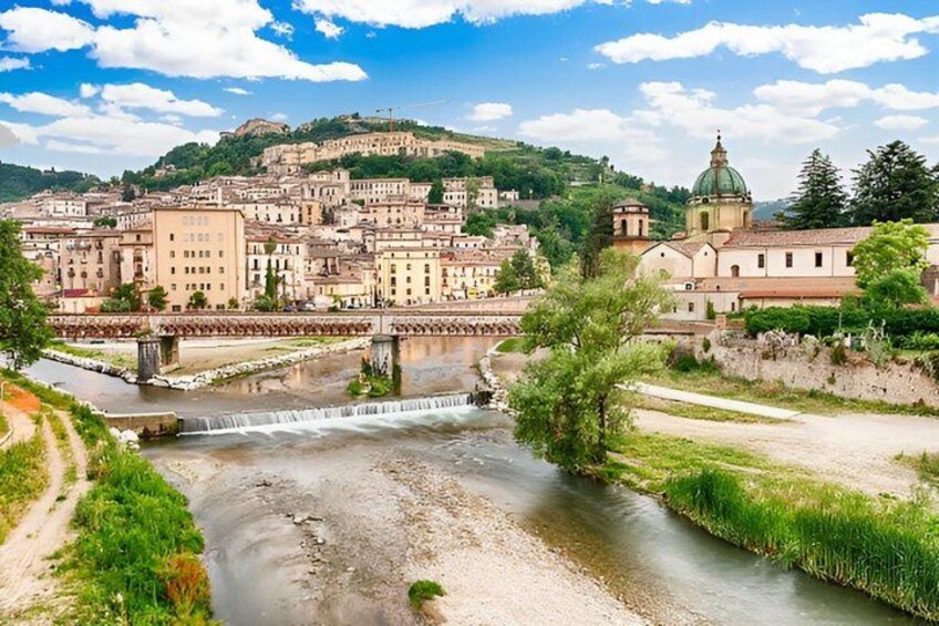 A river flowing through a town with a bridge, buildings, and a hill with a dome structure in the background. 5