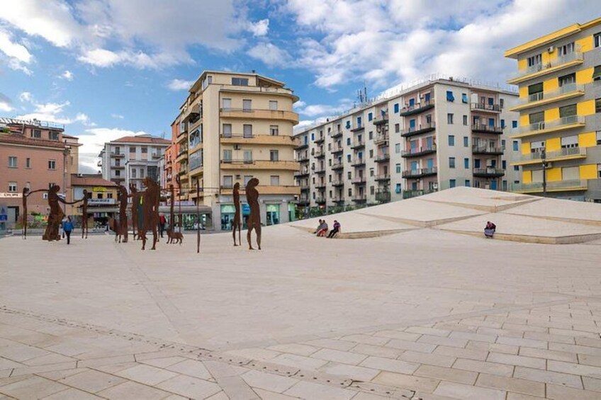 A public square with buildings, people, and a clear sky. 2